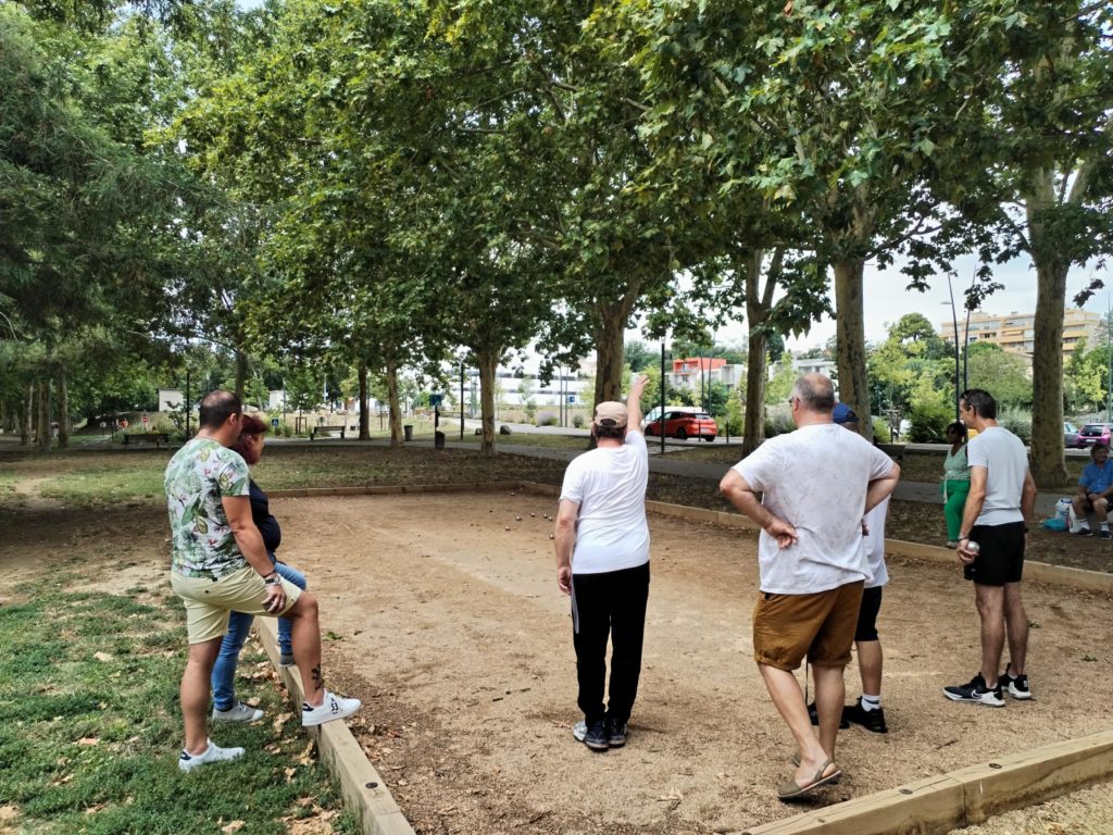 Six personnes de dos, sur le terrain de pétanque s'affrontent