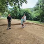 Trois personnes sur le terrain de pétanque dont un qui pointe.