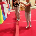 Une petite fille sur une poutre tenue par la main par une éducatrice