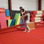 Une petite fille sur une poutre tenue par la main par une éducatrice