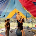 Une jeune sur la boule. L'animatrice lui tient les mains. Deux autres jeunes les regardent