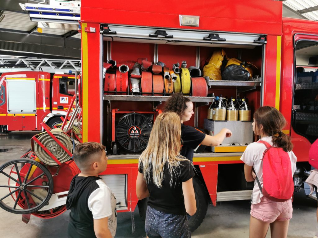 Les jeunes devant le camion de pompier. Un femme pompier leur donne des explications sur le fonctionnement du matériel