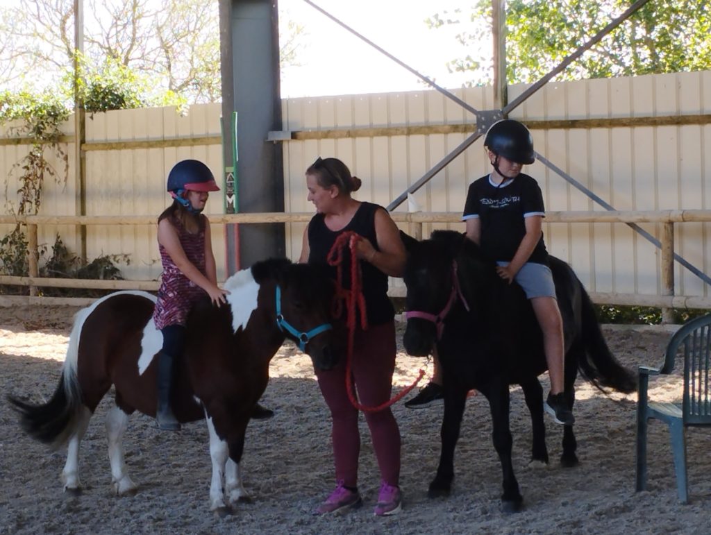 Deux jeunes sur deux poneys avec l'animatrice au milieu