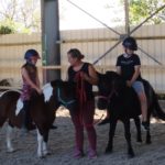 Deux jeunes sur deux poneys avec l'animatrice au milieu