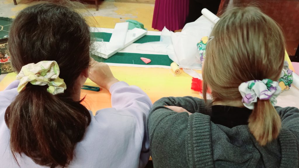 Deux jeunes filles de dos s'affairent à la table de couture