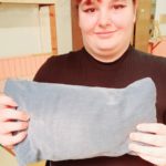 Une jeune fille montre son coussin gris uni achevé