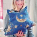 Une jeune fille montre son coussin avec des soleils, des lunes et des étoiles achevé