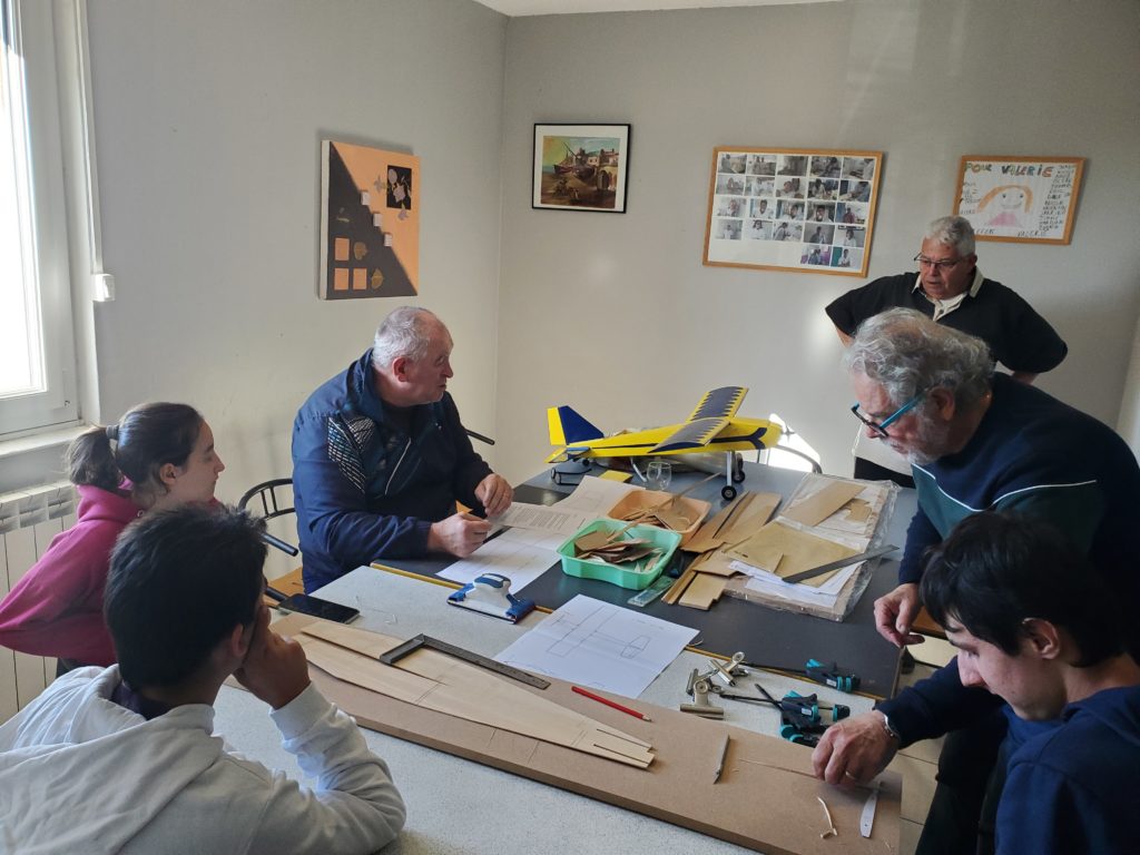 3 retraités et 3 jeunes autour d'une table font des travaux de découpe