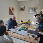 3 retraités et 3 jeunes autour d'une table font des travaux de découpe