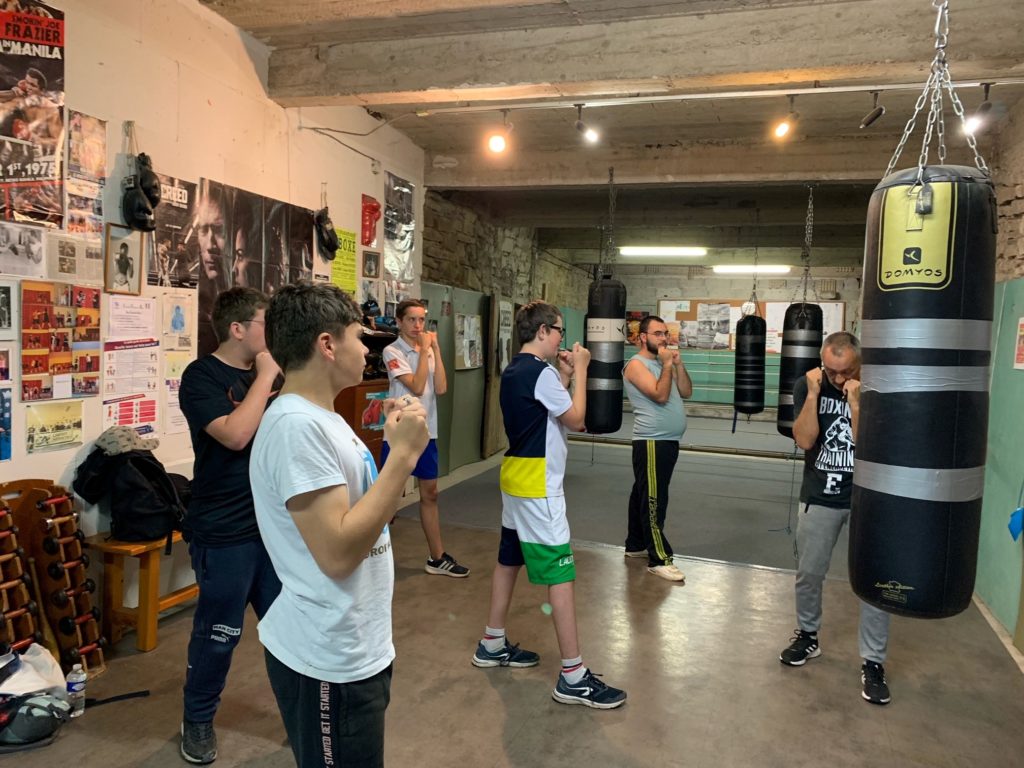 Dans la salle de sport, cinq jeunes apprennent à positionner les poings avec leur professeur