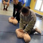 Deux jeunes effectuent un massage cardiaque aux mannequins. Un autre jeune les regarde.