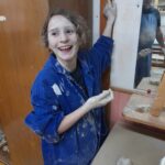 Une jeune fille fait de la poterie et a le visage et les bras plein d'argile. Elle explose de rire