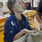 Une jeune fille fait de la poterie et a le visage et les bras plein d'argile.