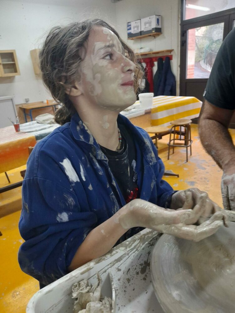 Une jeune fille fait de la poterie et a le visage et les bras plein d'argile.