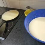 Une crêpe en préparation dans la poêle avec à côté la pâte à crêpes dans un saladier