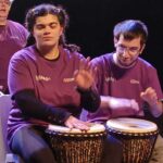 Deux jeunes aux percussions et en arrière plan une autre membre