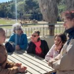 Trois jeunes et deux encadrantes assises autour d'une table en bois devant un enclos