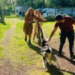 Une jeune fille sur un vélo tracté par un chien avec deux accompagnants pour la soutenir