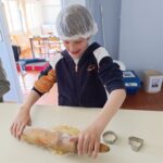 Un petit garçon avec une charlotte sur la tête et un rouleau à pâtisserie étale un sablé