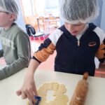 Un petit garçon avec une charlotte sur la tête découpe les sablés avec des emporte-pièces