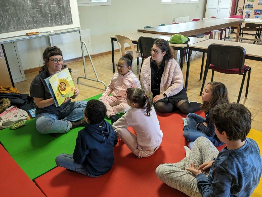 Les enfants et accompagnants assis autour de Anne qui fait la lecture