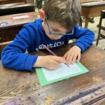 Un jeune garçon, en classe, écrit à la plume