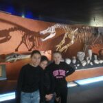 3 jeunes devant le squelette d'un dinosaure