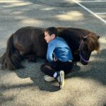 Un enfant de l'UEma est allongé contre un poney brun couché au sol