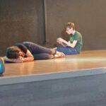 2 personnes sur scène, l'une allongée et l'autre assise