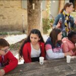 4 jeunes assis autour d'une table, se rafraichissent. En arrière plan, un encadrante leur sert un jus de fruit dans des gobelets