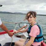 Une jeune fille souriante tient la barre l'avant du voilier