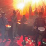 Les musiciens, au pied de la scène, tapent sur leurs percussions