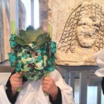 En gros plan, dans les locaux de Narbo Via un jeune portant une toge et le masque qu'il a confectionné