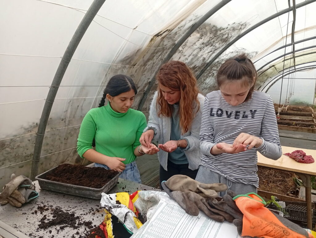 2 jeunes et leur éducatrice, dans la serre, effectuent des plantations