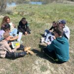 Assis en cercle sur la pelouse, le groupe écoute avec attention des explications données sur la biodiversité