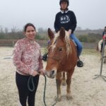 Un jeune accompagné est sur un poney qui est tenu par la bride par une monitrice