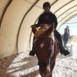 Au premier plan, un jeune sur un poney et en arrière plan, un autre jeune sur un poney, tenu par la bride par une monitrice