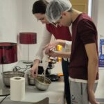Un jeune avec une charlotte et une accompagnatrice s'affairent en cuisine avec un mixeur