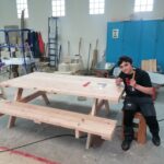 Un jeune, dans l'atelier, travaille sur la fabrication de la table