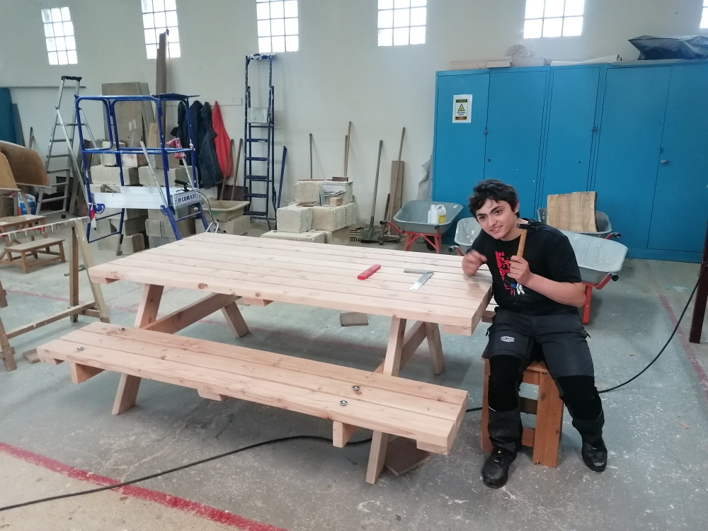 Un jeune, dans l'atelier, travaille sur la fabrication de la table
