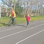 Un garçon court sur une piste d'athlétisme. A ses côtés, une personne sur un vélo.
