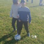 Un garçon les yeux bandés et le ballon aux pieds guidé par un autre garçon sur un terrain de foot