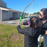 Une jeune fille tient un arc, aidée par son enseignante