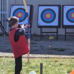 Un garçon en chasuble rouge tire à l'arc face à 3 cibles