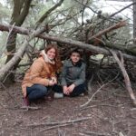 Un jeune et son éducatrice dans une cabane en branches construite par toute l'équipe