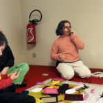 Une jeune fille, dans l'angle d'une pièce, assise au sol sur de la moquette rouge rapproche une forme ronde de son œil droit
