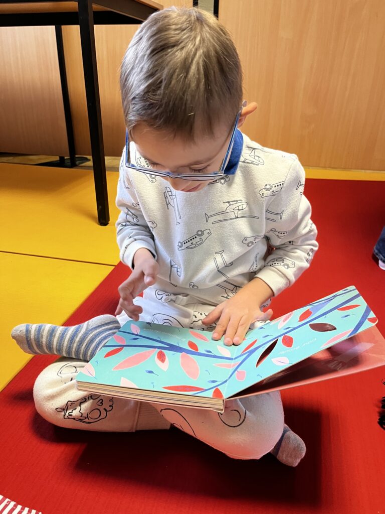 Un petit garçon assis sur un tapis rouge lit un livre