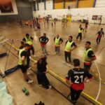 Au premier plan, sur la touche, une équipe est coachée. En arrière plan, sur le terrain du gymnase, des joueurs en plein effort