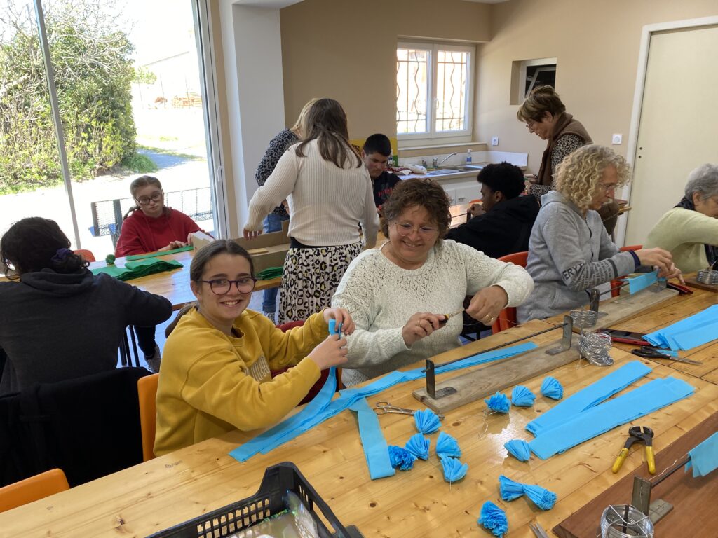 11 personnes (enfants et adultes) autour des tables confectionnent les éléments pour le corso fleuri