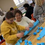8 personnes (enfants et adultes) autour des tables confectionnent les éléments pour le corso fleuri